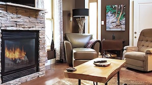Un salon avec une cheminée en pierre, des fauteuils en cuir, une table basse en bois et un tableau accroché au mur.