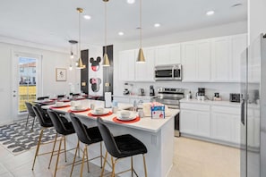 A modern kitchen with white cabinets, a central island with bar stools, and a dining area with a large window.