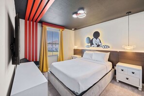 Habitación de hotel con cama, mesitas de noche, televisor de pantalla plana, una obra de arte colgada en la pared y ventana con cortinas.