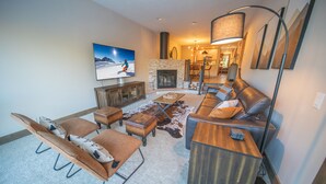 A modern living room with a fireplace, leather furniture, and a large flat-screen TV.