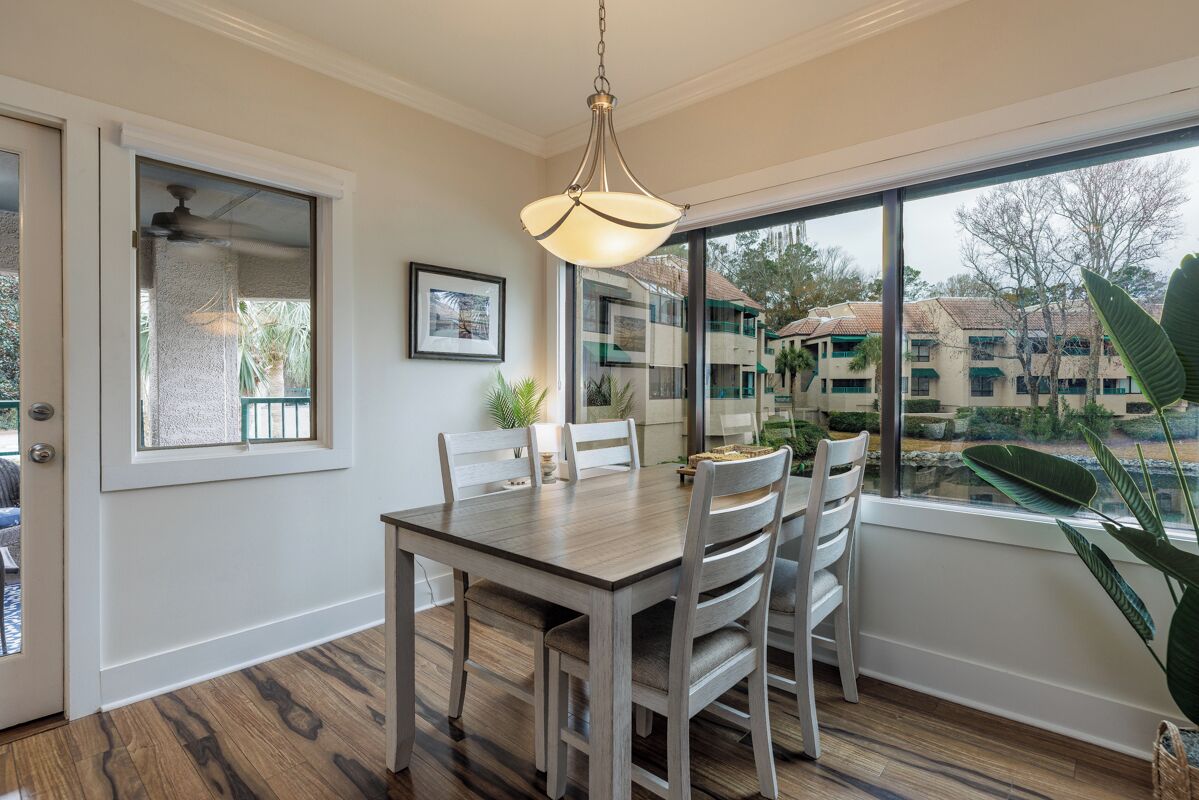 A dining area with a wooden table and chairs, a hanging light fixture, a window with a view of buildings, and a door with a glass panel.