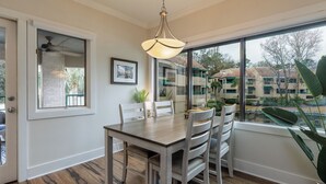 A dining area with a wooden table and chairs, a hanging light fixture, a window with a view of buildings, and a door with a glass panel.