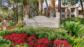A sign for 'The Anchorage at Shelter Cove' with a no bicycles or pedestrians on pavement sign, surrounded by lush greenery and palm trees.