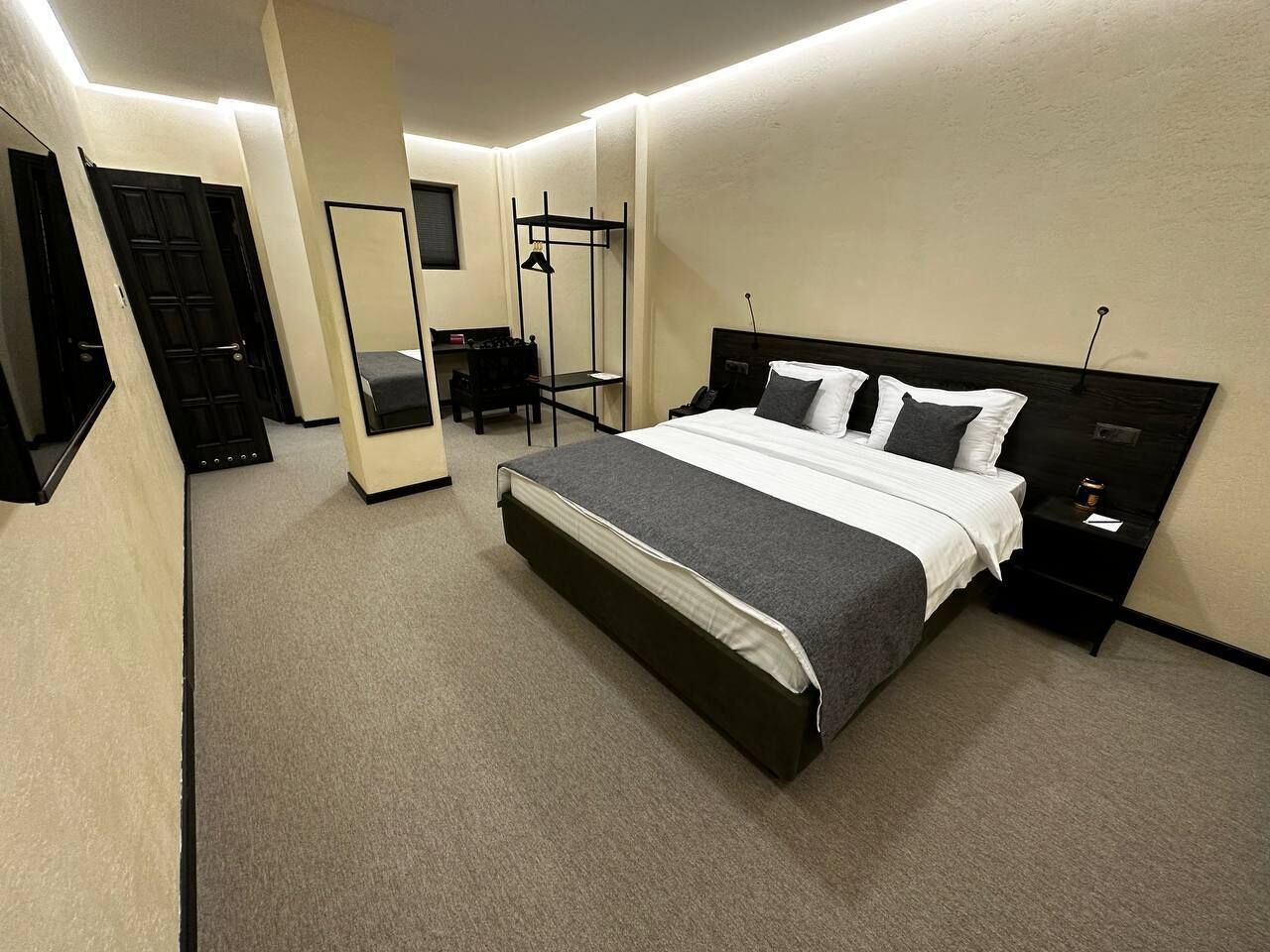 Un dormitorio ordenado con cama, mesitas de noche, armario y espejo.