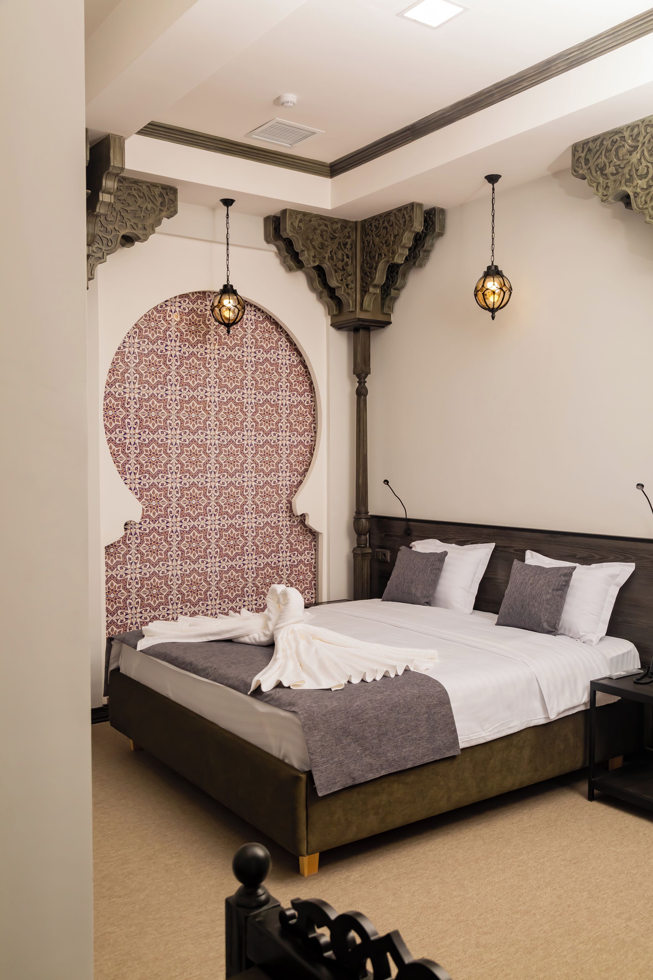 Un dormitorio con una cama grande, arcos ornamentales en la pared y lámparas colgantes.