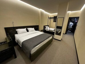 Une chambre d’hôtel moderne avec un grand lit, des tables de chevet, un miroir et une vue sur le couloir.