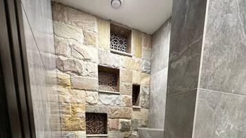 Un baño con pared de piedra, inodoro, ducha y secamanos.