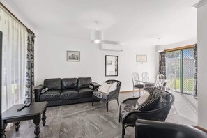 A living room with a black leather sofa, two wicker chairs, a small table, and a large window with a view.
