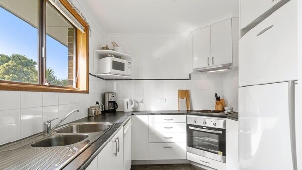 Eine moderne Küche mit weißen Schränken, einer Edelstahl-Spüle, einer Mikrowelle und einem Backofen.