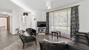 Ein Wohnzimmer mit einer Couch, zwei Sesseln, einem Fernseher und einem Fenster mit Vorhängen.