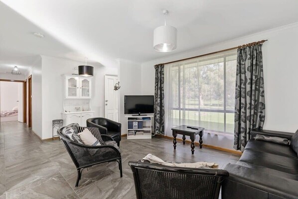 A living room with a sofa, two chairs, a television, and a window with curtains.