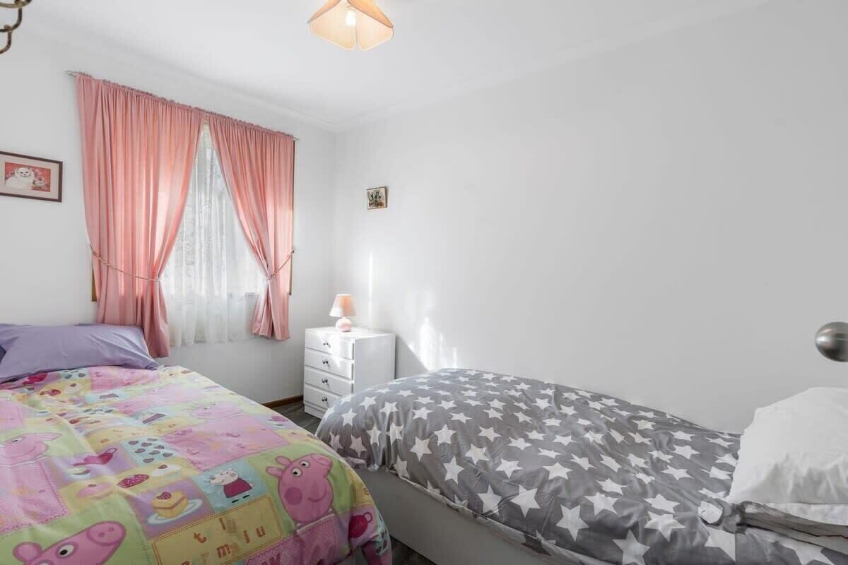 A bedroom with two beds, a nightstand, a lamp, and a window with curtains.