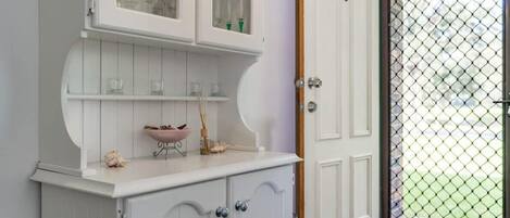 Un mueble blanco con puertas de cristal, un tazón rosa y un estante con objetos decorativos.