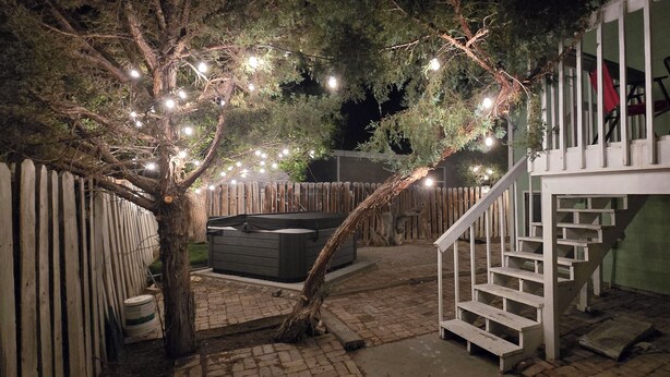 A backyard with a wooden fence, a hot tub, and a staircase leading to a balcony.