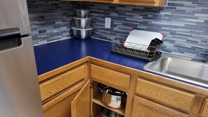 A kitchen with wooden cabinets, a blue countertop, a stainless steel sink, and a tiled backsplash.