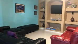 Un salón con un sofá negro y rojo, un televisor de pantalla plana montado en la pared y una pequeña bandera estadounidense.