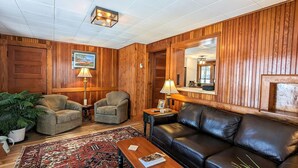 A cozy living room with wooden paneling, a leather sofa, two armchairs, a coffee table, and a rug. - Vintage & Modern Lodge-Lake Winnipesaukee water access w/ boat slip, dog welcome (Gilford)