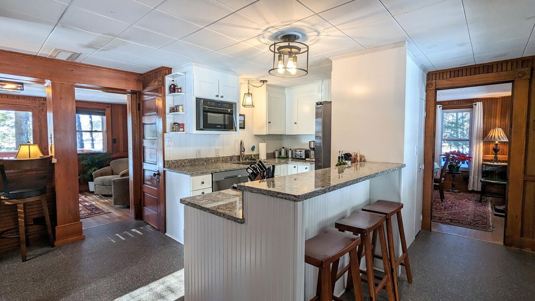 Una cocina moderna con armarios blancos, encimeras de granito y una isla central con taburetes.