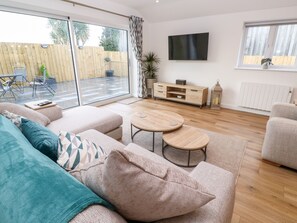 A modern living room with a sofa, two round tables, a TV, and a wooden cabinet. - Puffins Rest (Penzance)