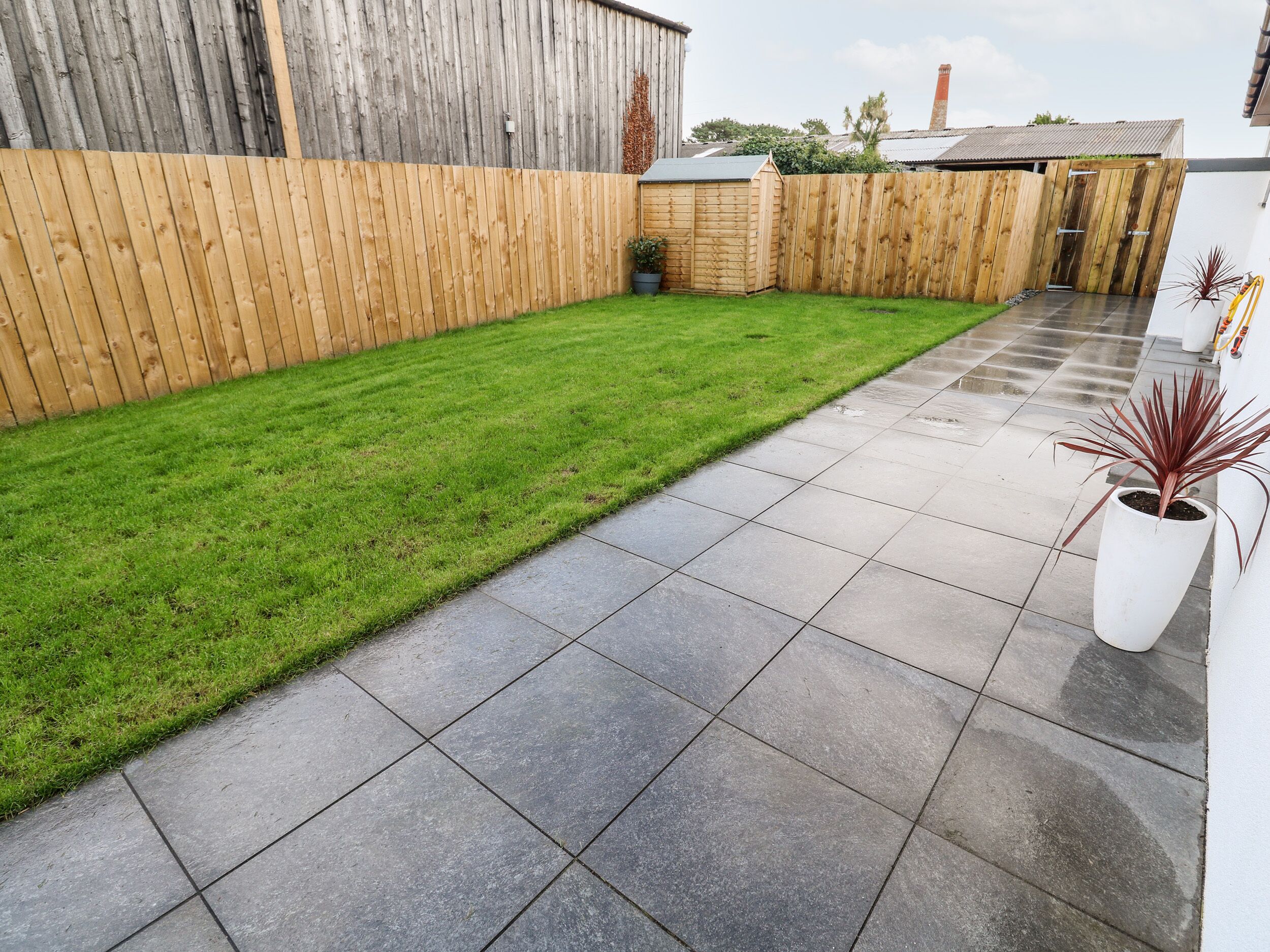 A backyard with a neatly trimmed lawn, a wooden fence, and a paved patio area.