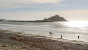 A beach with a castle-like structure in the distance, calm water, and a few people walking along the shore.