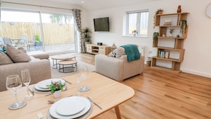 A modern living room with a dining table set for two, a sofa, a TV, and a bookshelf.