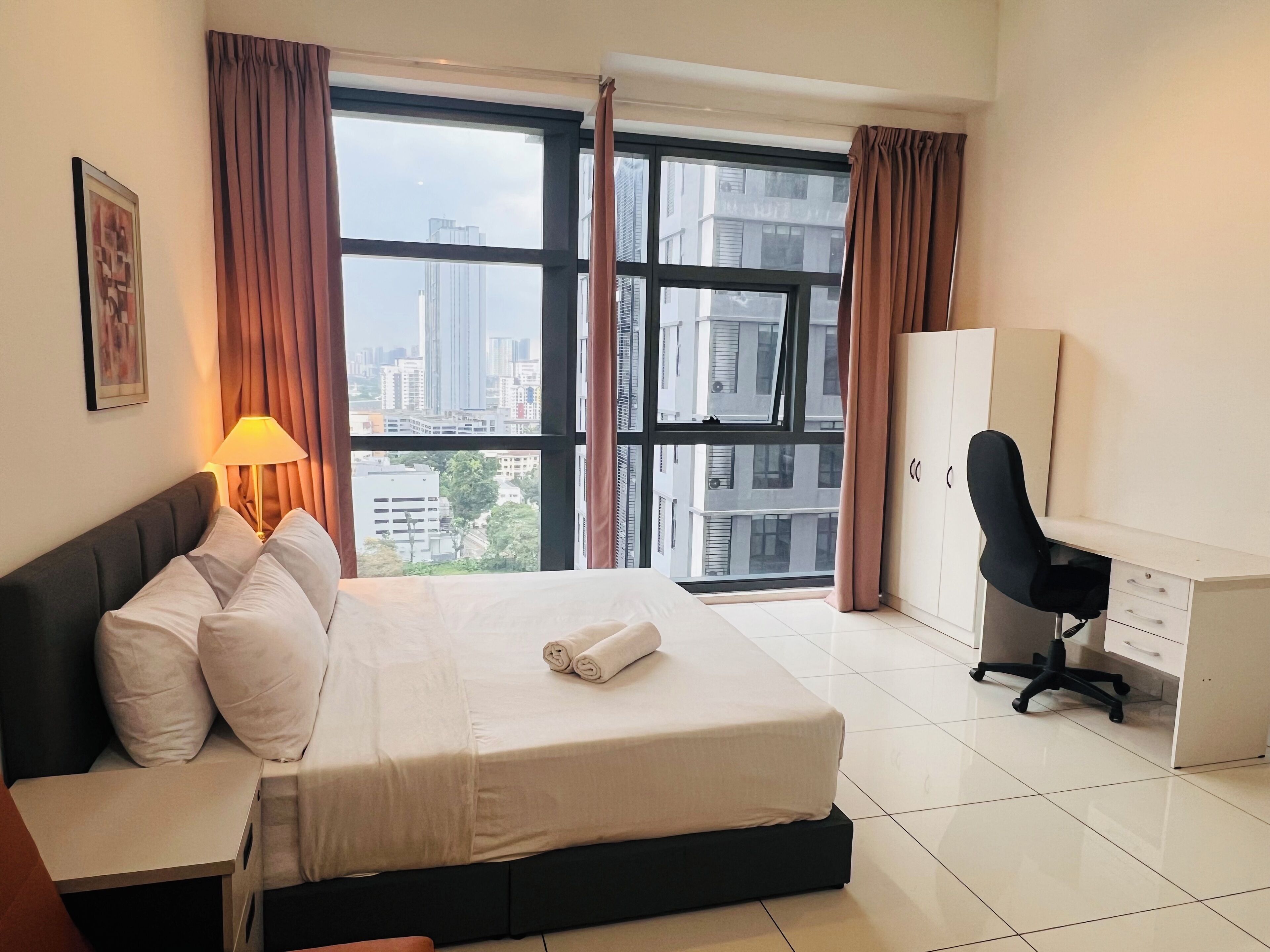 A hotel room with a bed, a desk, and a view of tall buildings.