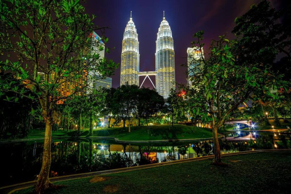 De Petronas Twin Towers 's nachts, omringd door bomen en een waterpartij die de torens weerspiegelt.