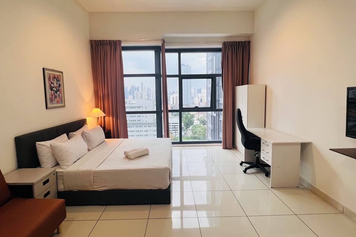 Een moderne hotelkamer met een groot bed, een bureau, een stoel en uitzicht op de stadslijn door grote ramen.