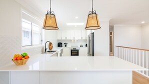 A modern kitchen with white cabinetry, a large island, stainless steel appliances, and two wicker pendant lights. - Bel Air, 8A Ocean Ave - pet friendly, water views and air con (Anna Bay)