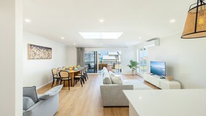 A modern living room with a dining area, a sofa set, a TV, and a large window. - Bel Air, 8A Ocean Ave - pet friendly, water views and air con (Anna Bay)