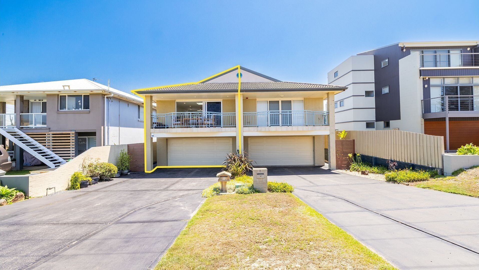 A modern two-story residential building with a central balcony, a garage, and a well-maintained front yard.