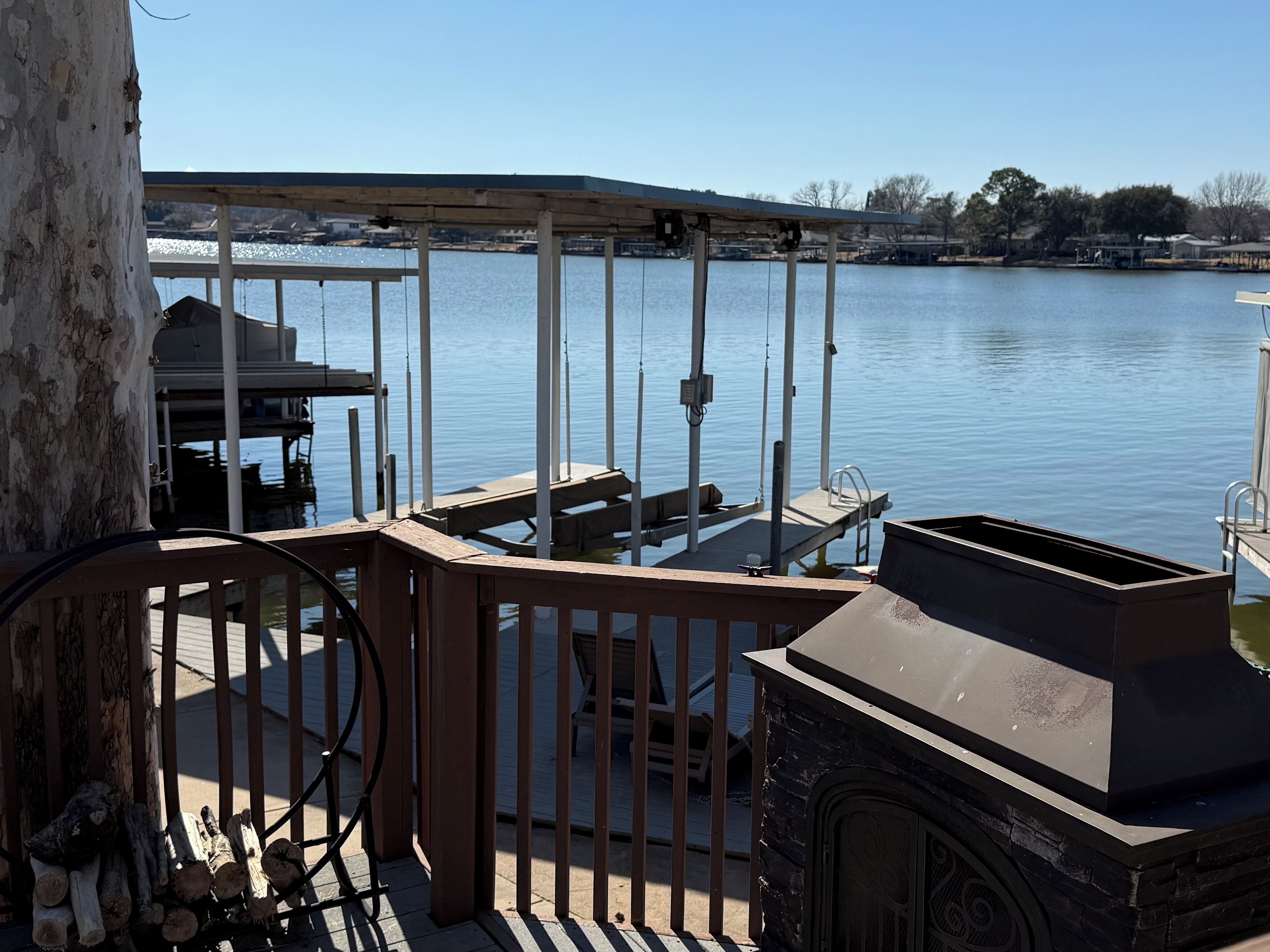 A wooden deck with a barbecue grill, a table, and chairs overlooking a calm lake.
