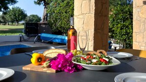 An outdoor dining area with a pool, a bottle of wine, and a plate of food. - Villa HG21 Olympus - Two Bedroom Villa, Sleeps 4 (Kouklia)