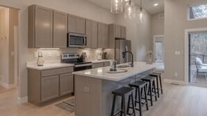 A modern kitchen with a central island, bar stools, pendant lighting, and a view to the outdoors.