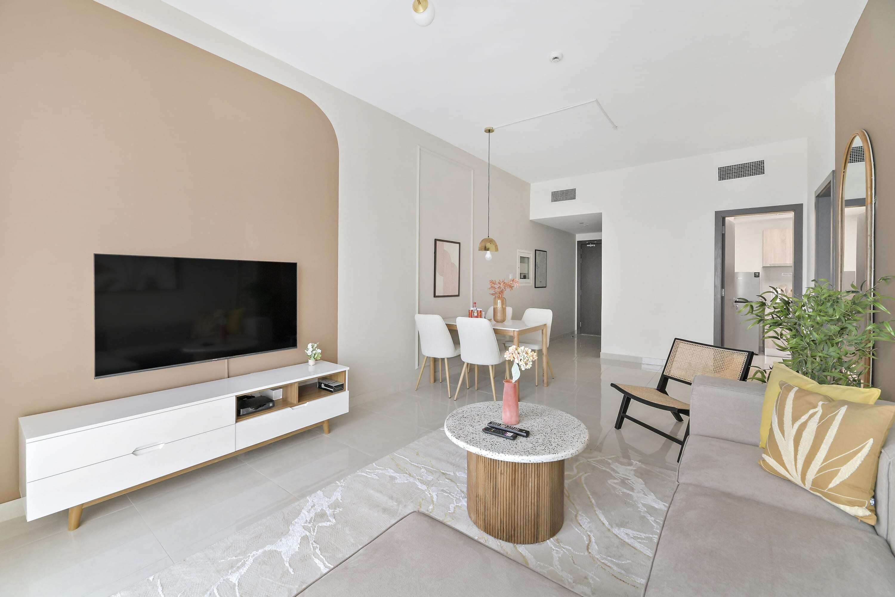 A modern living room with a flat-screen TV, a white entertainment unit, a round coffee table, and a sofa with decorative pillows.