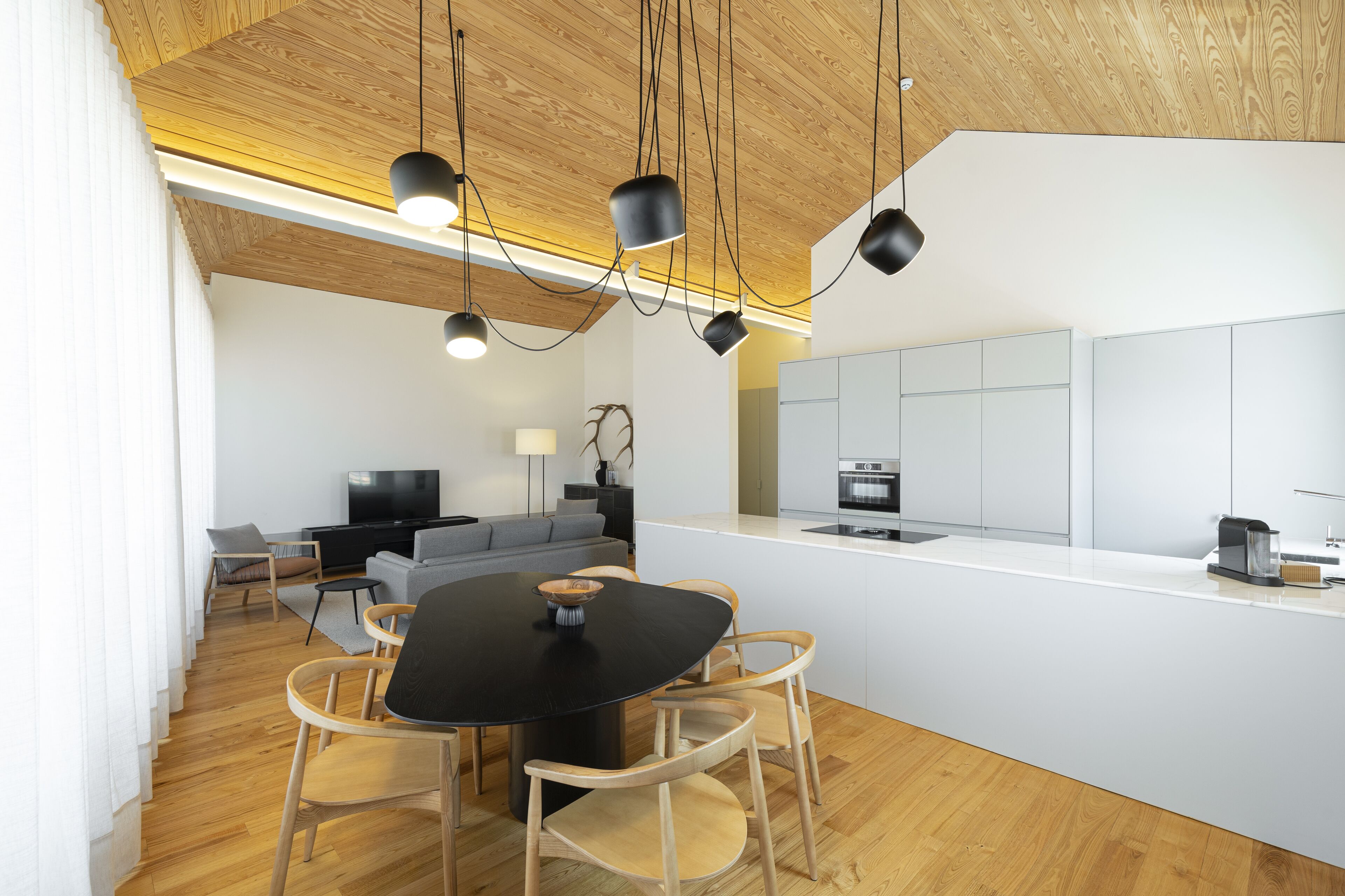 Une cuisine moderne avec des meubles blancs, un îlot central et un coin repas comprenant une table noire et des chaises en bois.