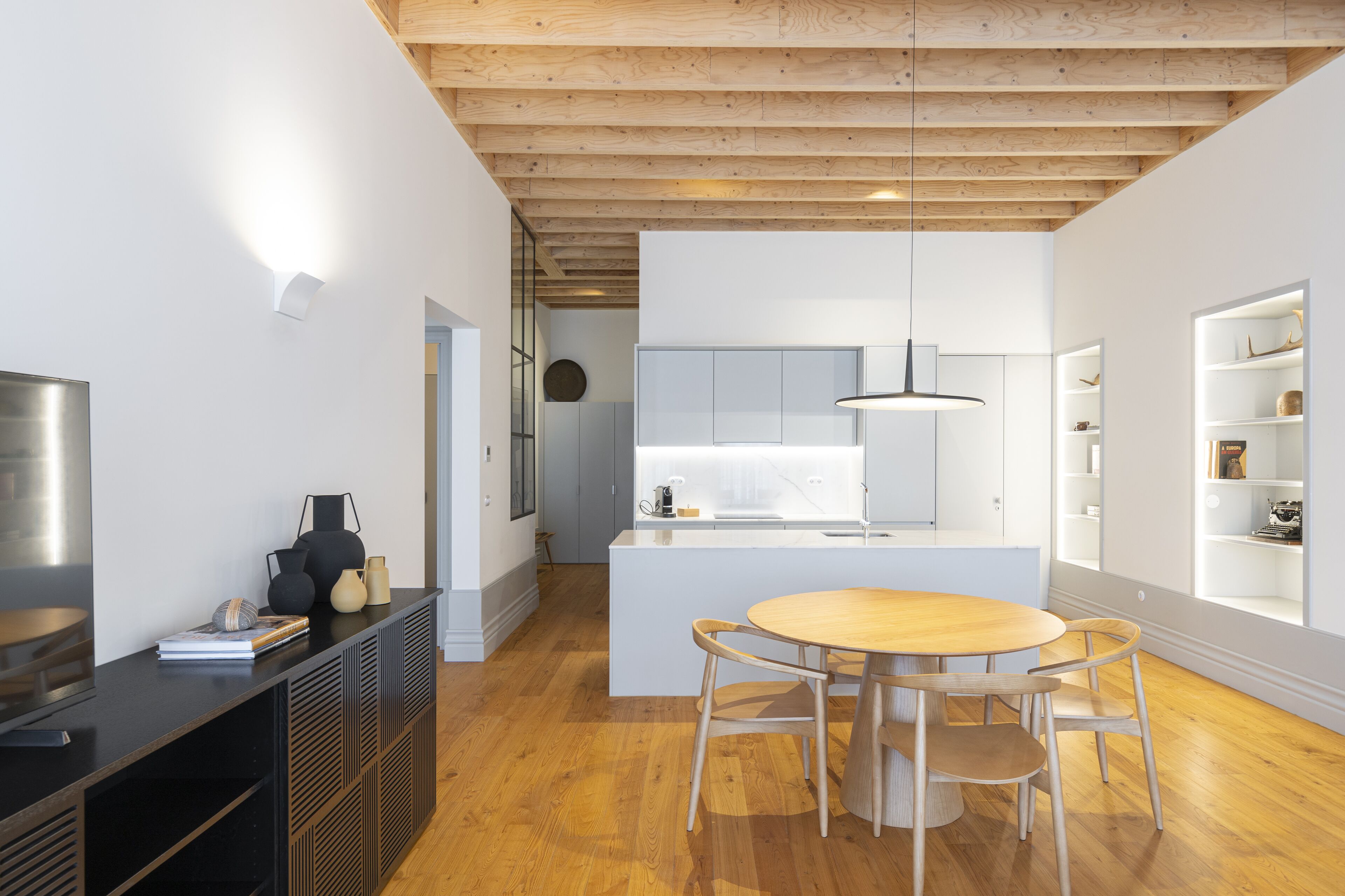 Una cocina moderna con armarios blancos, una isla central con asientos y suelo de madera.