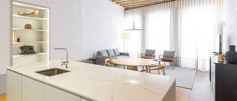 A modern kitchen with a marble countertop, wooden ceiling beams, and a built-in shelf with decorative items.
