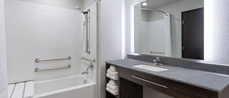 A modern bathroom with a walk-in shower, grab bars, a large mirror, and a dark wood vanity with a sink.