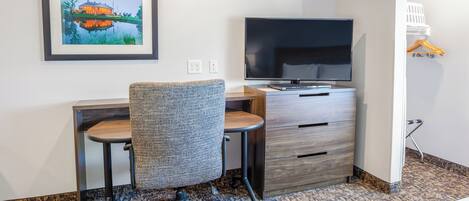 Una habitación de hotel con escritorio, silla, televisión y un cuadro en la pared.