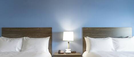 A hotel room with two beds, a nightstand with a lamp, and a phone.