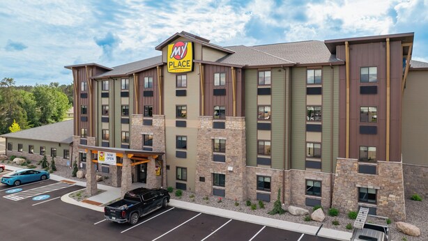A multi-story hotel with a prominent 'My Place' sign, a parking lot with several cars, and a landscaped entrance area.