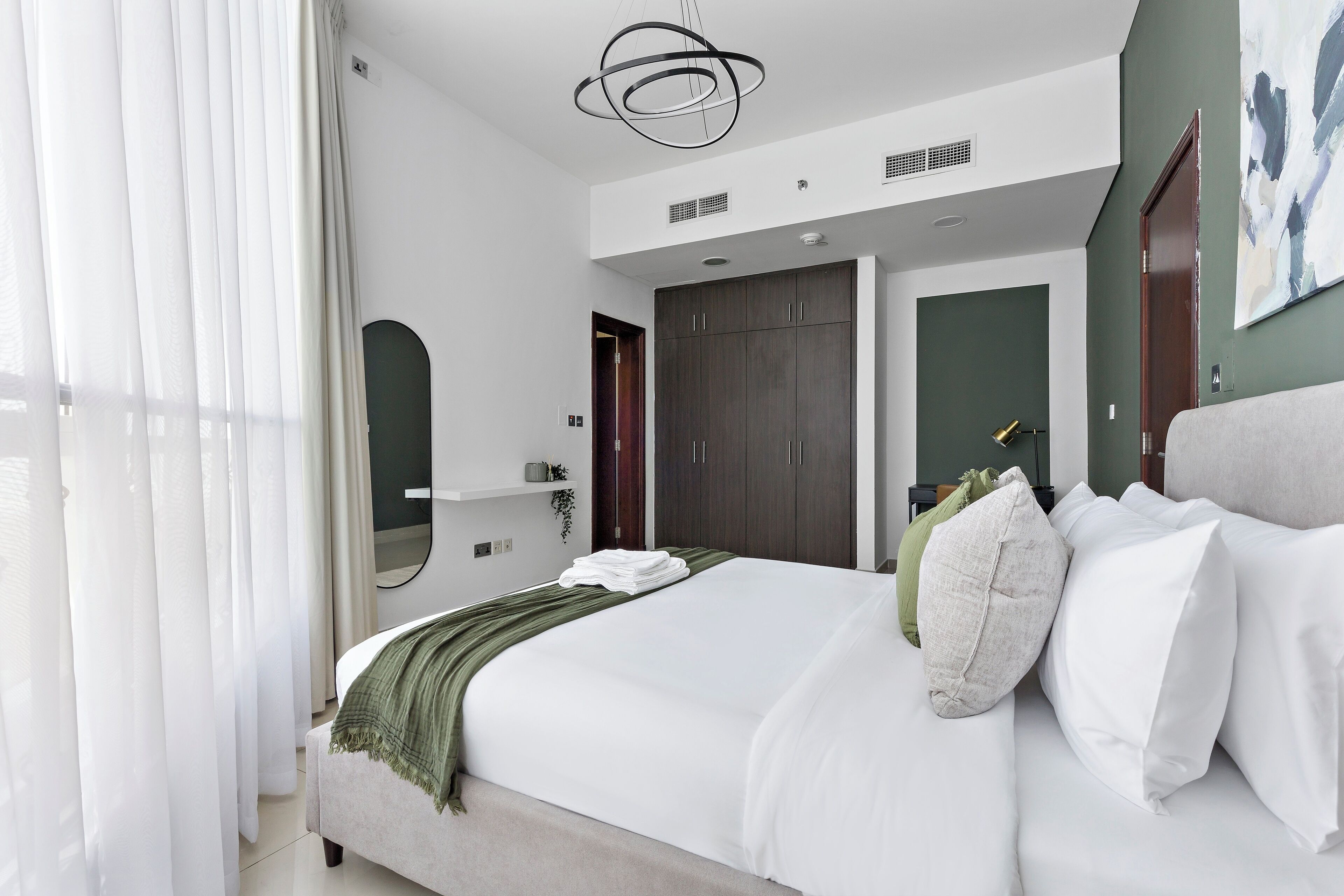 Une chambre moderne avec un grand lit, un plaid vert et un miroir au-dessus du lit.