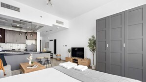 Une chambre d’hôtel moderne équipée d’une kitchenette, d’un lit avec une couverture grise, d’une table basse en bois et d’une armoire grise.