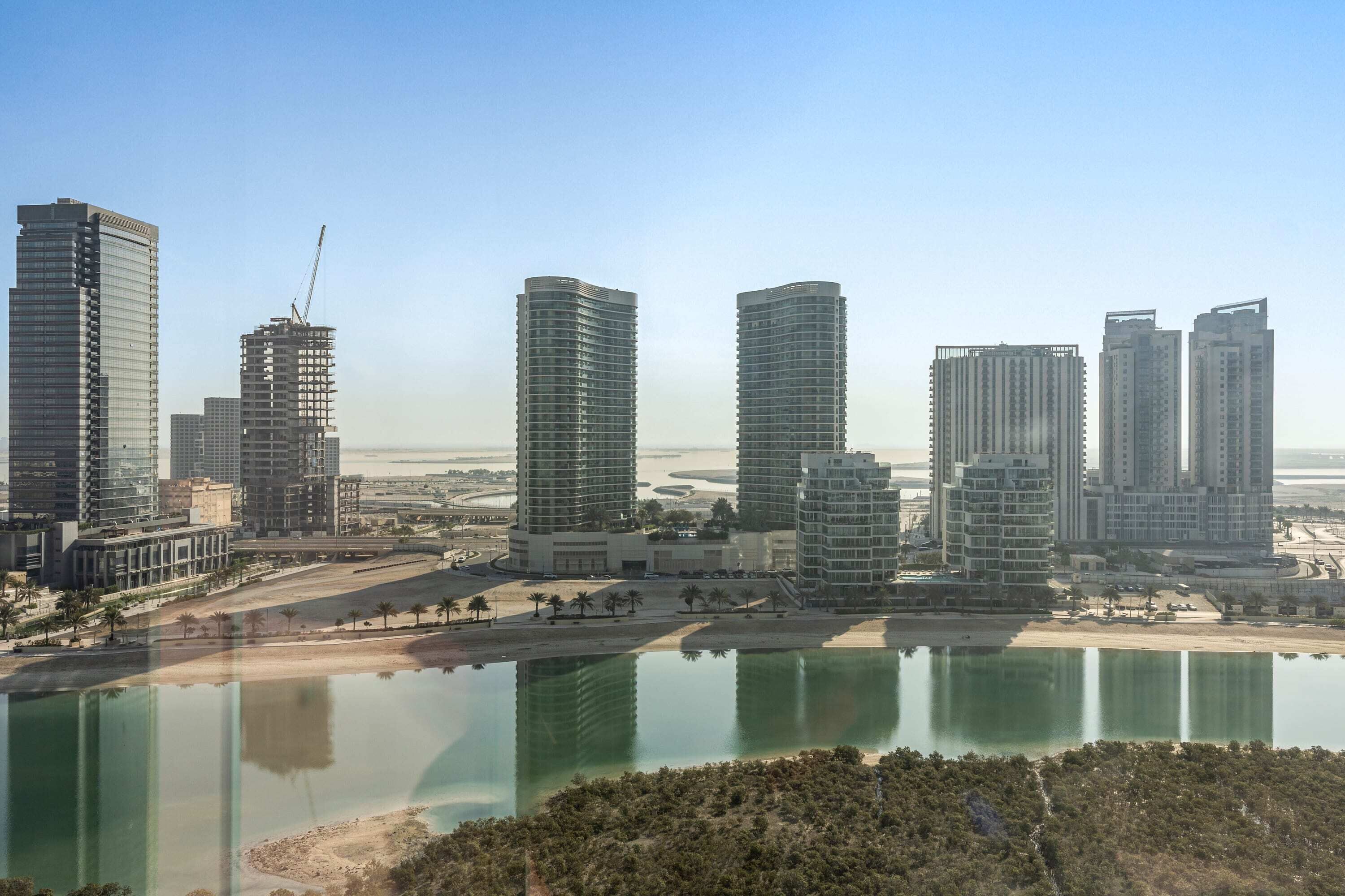 A high-rise urban area with multiple modern buildings, a large body of water, and a construction crane visible.