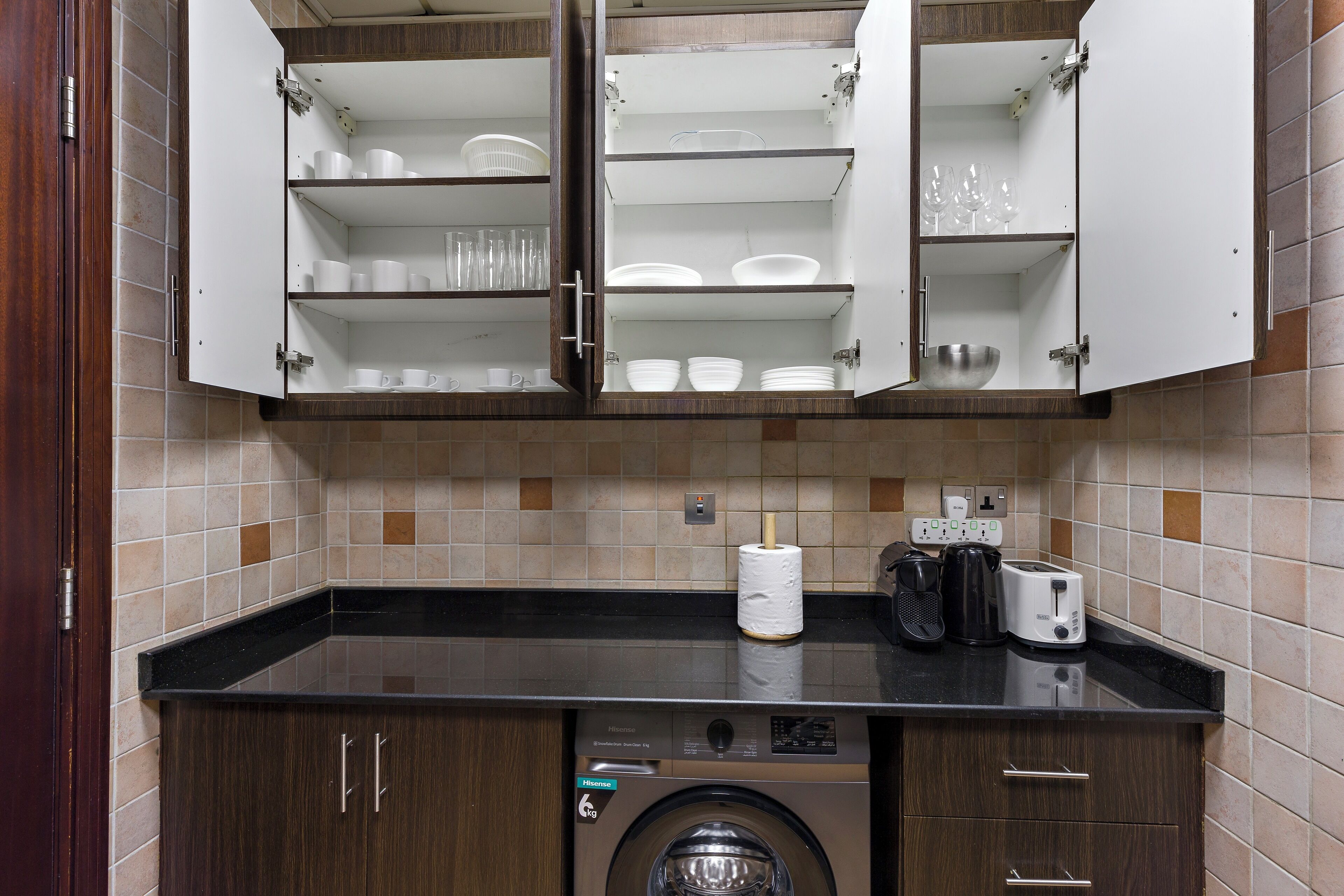 A kitchen with a washing machine, a coffee maker, and a toaster on the counter.
