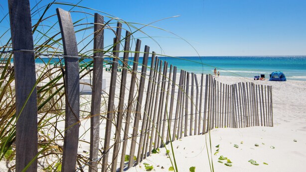 A beach with a wooden fence, a tent, and a clear blue sky.