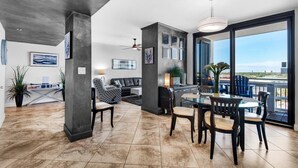 A spacious living area with a dining table and chairs, a sofa, and a balcony with a view.