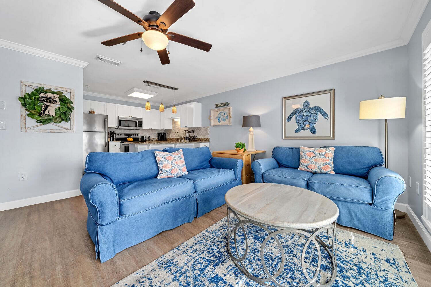 A living room with two blue sofas, a round coffee table, and a ceiling fan.